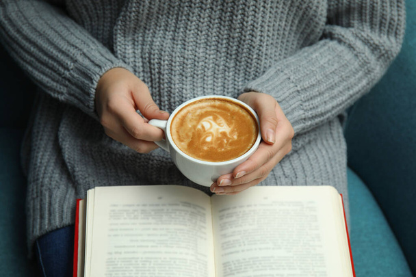 Woman with cup of coffee reading book at home, closeup - Foto, imagen