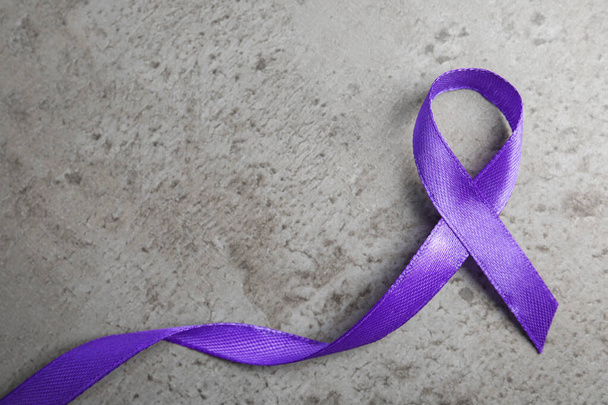 Purple ribbon on grey stone background, top view. Domestic violence awareness - Photo, Image