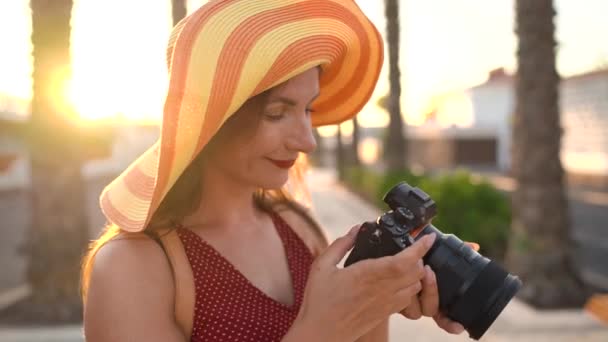 Φωτογράφος τουρίστας γυναίκα με ένα μεγάλο κίτρινο καπέλο λήψη φωτογραφιών με την κάμερα σε ένα όμορφο τροπικό τοπίο στο ηλιοβασίλεμα - Πλάνα, βίντεο