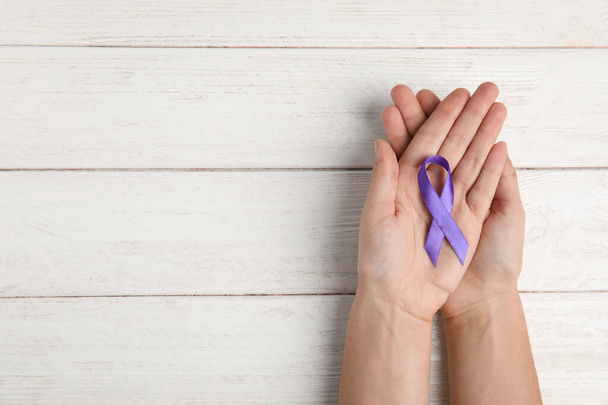 Woman holding purple ribbon on white wooden background, top view with space for text. Domestic violence awareness - Foto, Imagen