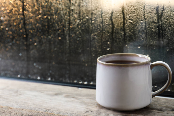 Cup of hot tea on wooden window sill. space for text. Rainy weather - Foto, Imagen
