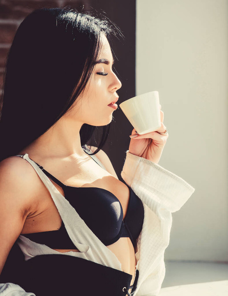 My morning coffee and quiet time routine. Sexy woman drinking healthy morning drink at window. Sensual girl enjoying her aromatic morning coffee. Coffee wakes her up in the morning - Valokuva, kuva