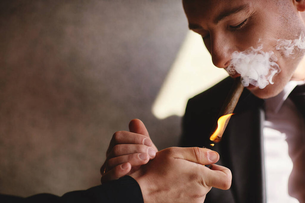 tyylikäs mies yllään puku ja valkoinen paita tupakointi sikari sisätiloissa ammuttu, lähikuva, valikoiva keskittyä. sikarin savu
 - Valokuva, kuva