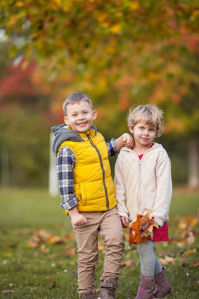 Little boy hugs a girl. Portrait of happy children in bright, autumn clothes. Warm and bright autumn. - Фото, зображення