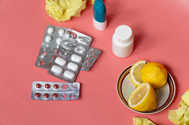 concept van koude: gesneden citroen met koude pillen en neusspray op roze achtergrond - Foto, afbeelding