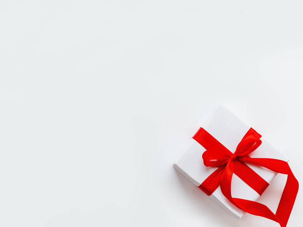 Present in white wrapping paper on white backdrop. Holiday gift with red ribbon and bow. Copy space. - 写真・画像