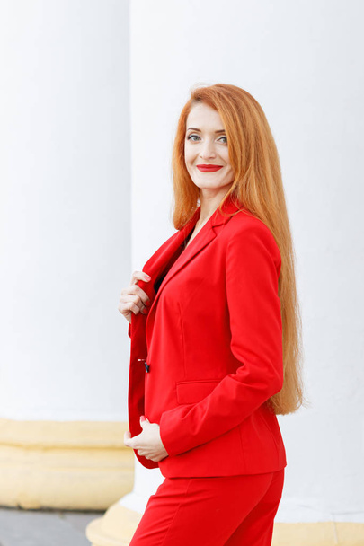 όμορφη κοπέλα με κόκκινα μαλλιά ντυμένη με κόκκινο κοστούμι. Λεωφορείο - Φωτογραφία, εικόνα