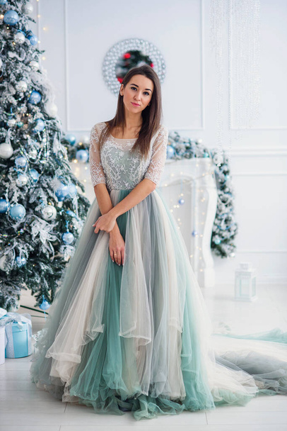 Attractive woman in tender evening dress near Christmas tree at cozy home. Happy winter holidays concept. - Fotó, kép