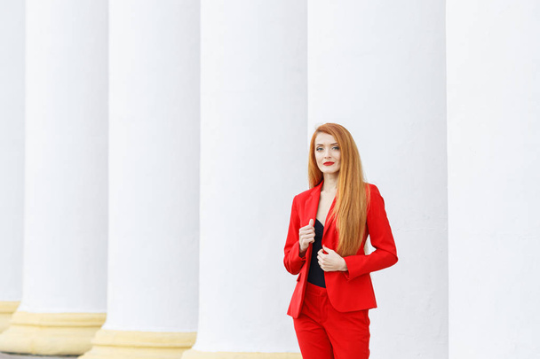 όμορφη κοπέλα με κόκκινα μαλλιά ντυμένη με κόκκινο κοστούμι. Λεωφορείο - Φωτογραφία, εικόνα
