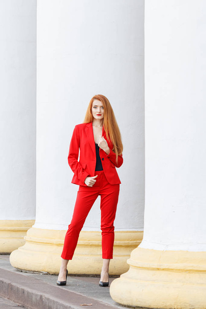 beautiful girl with red hair dressed in a red business suit. Bus - 写真・画像