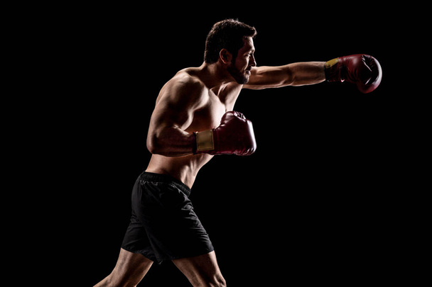 Strong muscular man with boxing gloves throwing a punch - Foto, Imagen