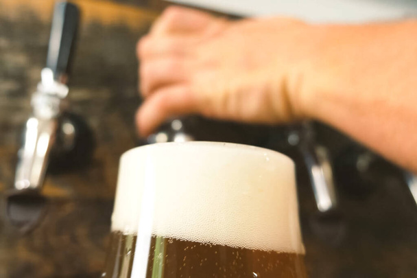Pouring beer into a glass from the tap at bar. Beer bottling. - Photo, image