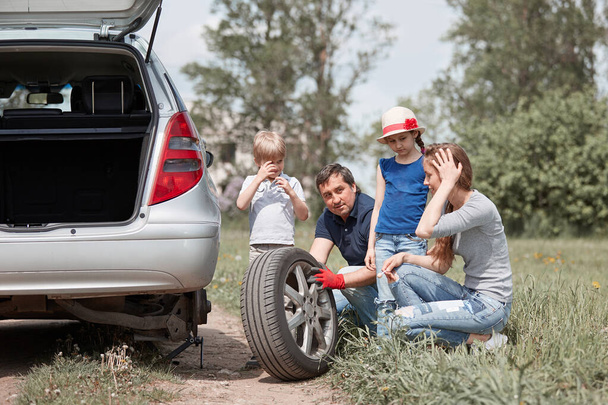 οικογένεια με δύο παιδιά αντικαθιστούν το ελαστικό του οικογενειακού αυτοκινήτου. - Φωτογραφία, εικόνα