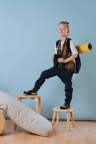Retrato de un niño pequeño con binoculares escalando taburetes, jugando al excursionista en casa
 - Foto, imagen