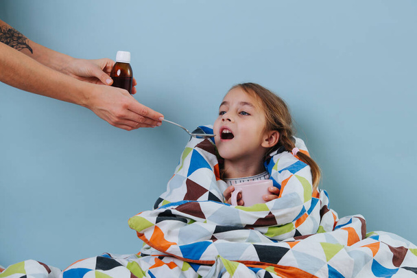 Sick little girl with common cold is sitting in bed, taking medicine - Photo, Image