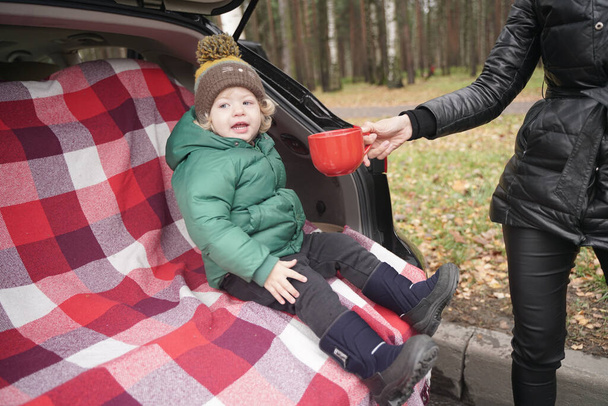 Familie avontuur - familie op herfstkamp. jong schoonheid mam en weinig kind had picknick in achterzijde van auto in de buurt van de herfst park - Foto, afbeelding