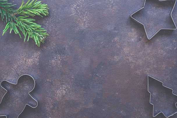 Christmas holiday background with cookie cutters, evergreen fir branch on vintage style dark background. Concept of holiday coziness, top view, flat lay, copy space for text. - Fotó, kép