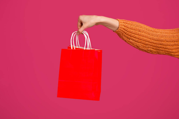 Žena ruka drží prázdný červený nákupní taška přes růžové pozadí - Fotografie, Obrázek