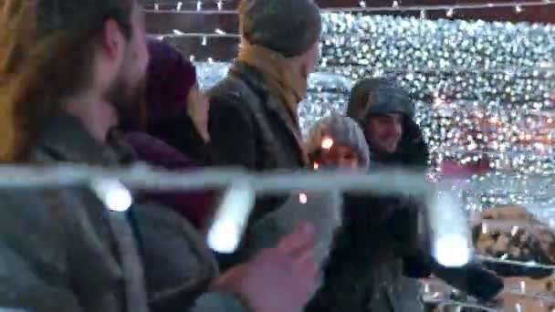 Ystävät pitää hauskaa kävely sparklers juhlava valaistus tunneli luminen talvi-iltana. Onnellinen ryhmä ihmisiä hengailee joulumarkkinoilla. Garland lamput, karuselli valot taustalla
. - Materiaali, video
