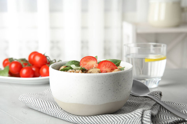 Delicious buckwheat porridge with mushrooms and tomato on table indoors - Foto, afbeelding