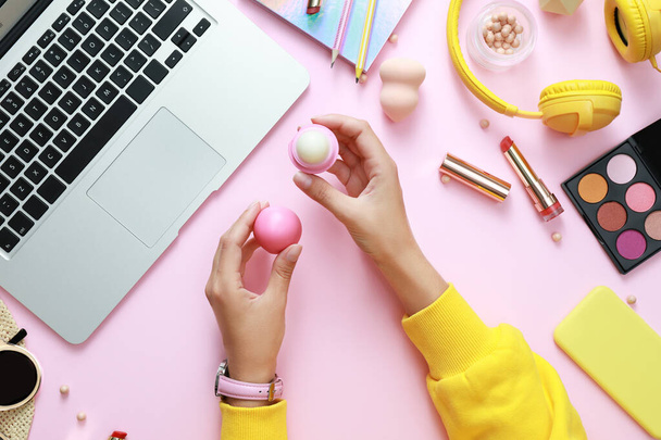 Young beauty blogger with lip balm near laptop and accessories on light pink background, top view - Фото, зображення