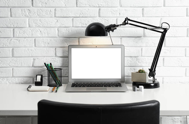 Moderni työpaikka kannettava tietokone ja lamppu pöydällä lähellä tiiliseinää. Suunnittelutila
 - Valokuva, kuva