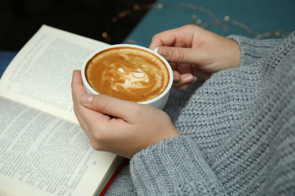 Woman with cup of coffee reading book at home, closeup - 写真・画像