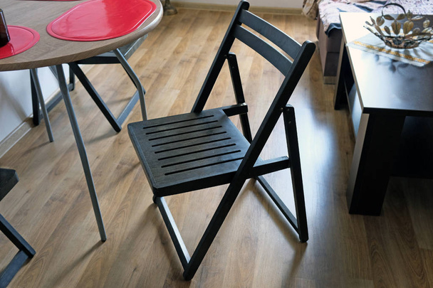 Ein schwarzer Holzstuhl in der Mitte der Küche gegen ein braunes Laminat und Küchenmöbel: ein Stuhl, ein runder Holztisch mit grauen Metallbeinen. Küchenklappstuhl. Möbel für zu Hause. - Foto, Bild