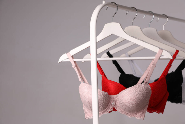 Hangers with beautiful lace bras on rack against grey background. Stylish underwear - Foto, Imagem