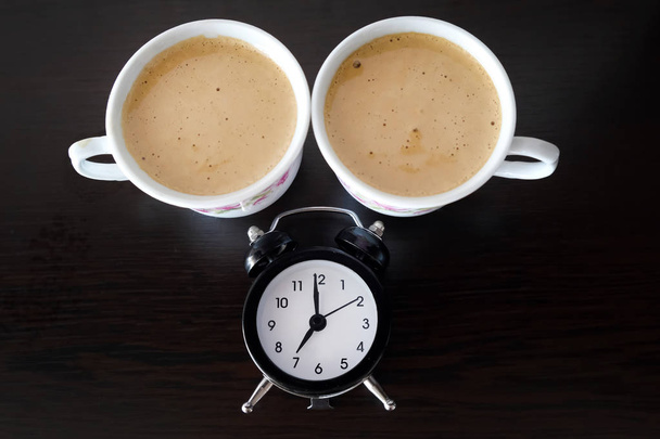 Концепція часу пити каву. Дві маленькі чашки кави і чорний будильник на столі вид зверху
. - Фото, зображення