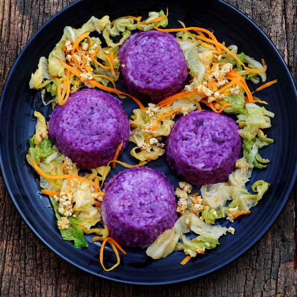 schwarzer Teller mit violettem Reisgericht und Gemüse, lecker vegan - Foto, Bild