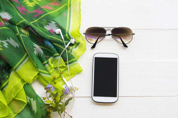 telefone celular, óculos de sol e lenço verde de estilo de vida mulher relaxar no arranjo temporada de inverno flat lay estilo no fundo branco de madeira
 - Foto, Imagem