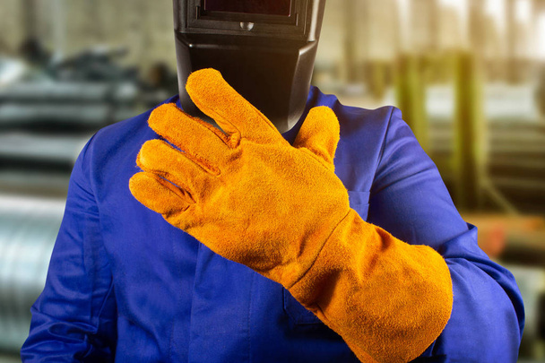 Svářečka v oranžových rukavicích a masce stojící v továrně zblízka. - Fotografie, Obrázek