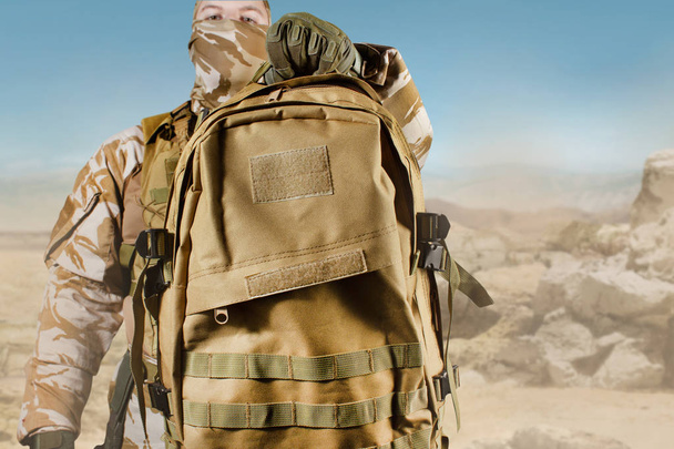 Soldier in uniform holding backpack on desert background. - Photo, Image