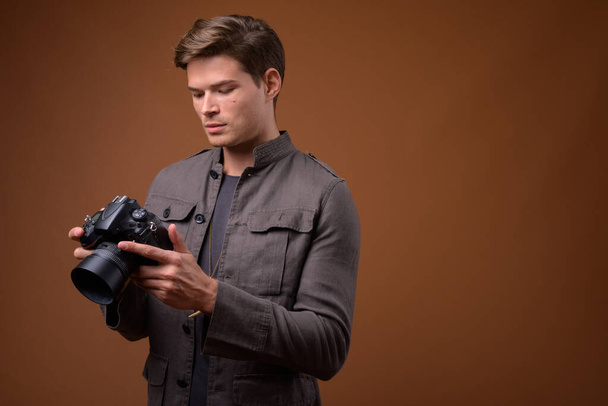 Studio shot of young handsome man as photographer with camera - Foto, afbeelding