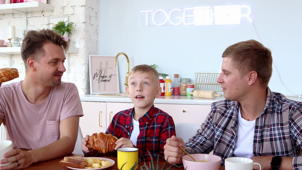 Χαρούμενη οικογένεια γκέι. Δύο πατεράδες και γιος τρώνε πρωινό στην κουζίνα.. - Πλάνα, βίντεο