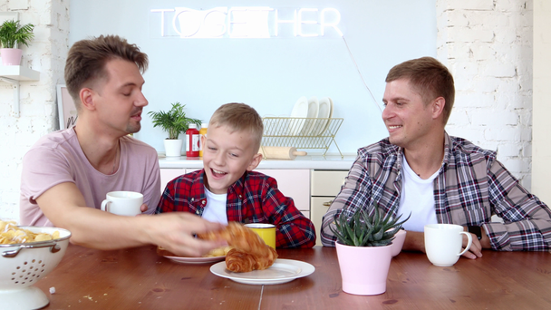 Happy gay family two fathers and son are having breakfast in the kitchen. - Footage, Video