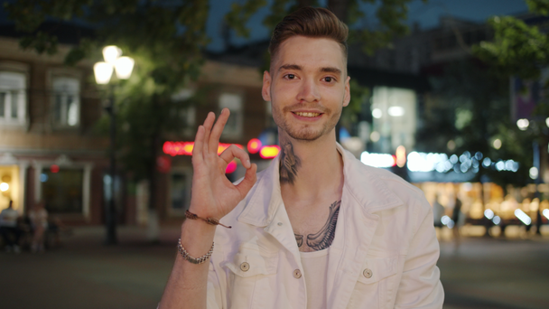 Portret wytatuowanego faceta pokazującego Ok gestem dłoni uśmiechającego się patrząc na aparat na zewnątrz - Materiał filmowy, wideo