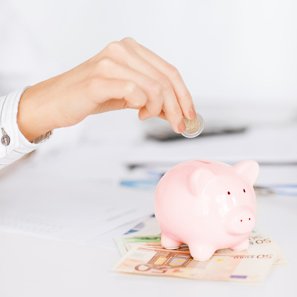 Woman hand putting coin into small piggy bank - Photo, image