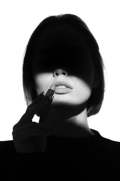 Fashion advertising portrait of a young beautiful girl using lipstick. Black and white silhouette with epic light. - Foto, imagen