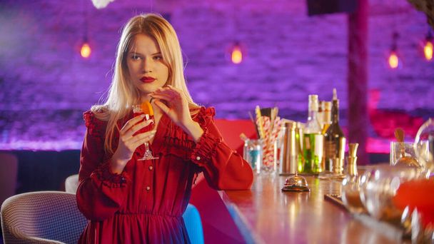 Gyönyörű fiatal nő ül a pultos állvány mellett - szalmaszálból iszik egy italt és oldalra néz - Fotó, kép