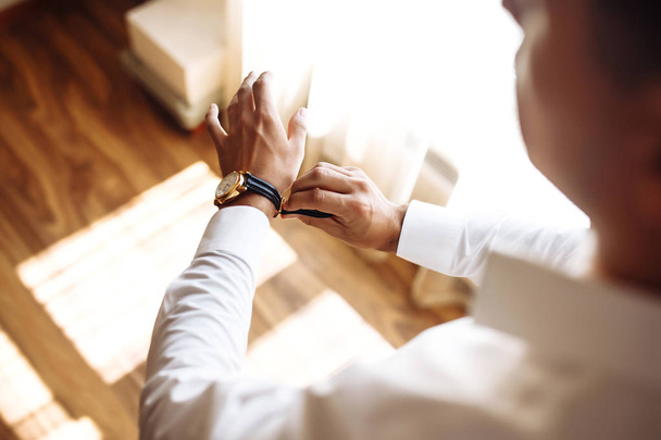 Men's wrist watch, the man is watching the time. Businessman clock, businessman checking time on his wristwatch. Groom's hands in a suit adjusting wristwatch, wedding preparations, groom accessories. - 写真・画像