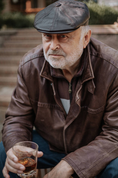 Elderly man with beard in leather jacket sits in yard - Fotó, kép