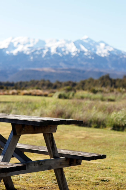 ニュージーランドのトンガリロ国立公園に雪をかぶった山々とピクニックテーブルとベンチ - 写真・画像