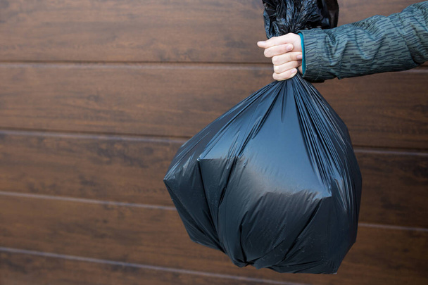 The guy holds a black trash bag close-up. - Фото, изображение