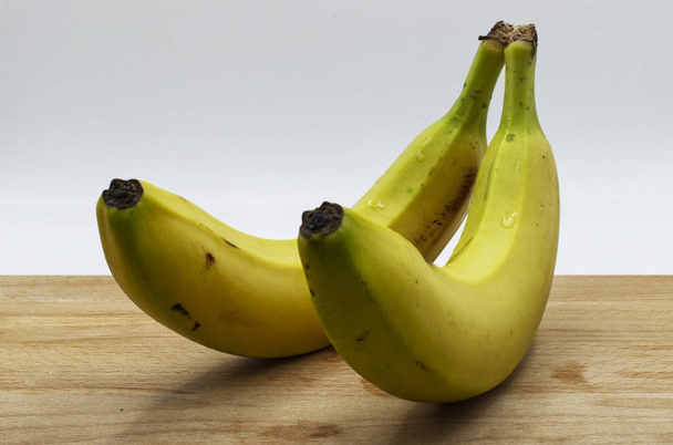 Bananas on wooden table, white background - Foto, Imagen