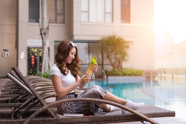 Young Asian woman sitting on deckchair and drinking juice near swimming pool - Φωτογραφία, εικόνα