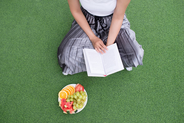Розслаблюючі моменти, молода жінка читає книгу, сидячи на траві
. - Фото, зображення