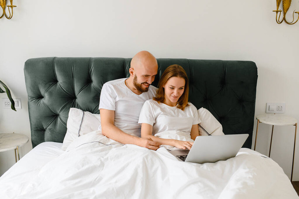 young couple using laptop together in bed  - Фото, изображение