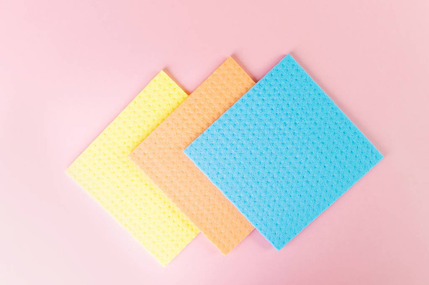 New rags for wet cleaning. Blue, yellow and orange rags on a pink background. The concept of cleanliness, minimalism. Place for text. - Photo, Image